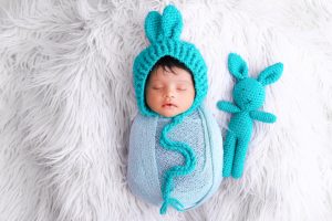 A baby sleeping in a blue knitted bunny hat.