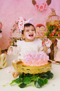 A baby girl is sitting in front of a cake in pink dress.