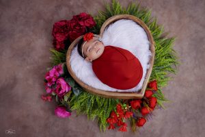 A baby is laying in a heart shaped frame with flowers.