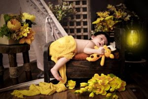 A baby sleeping in a wooden box with yellow flowers.