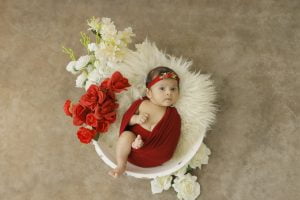 A baby girl in a red dress laying in a bowl with flowers.