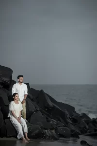A man and woman are sitting on rocks near the ocean.