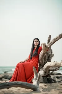 A woman in a red dress sitting on a driftwood on the beach.