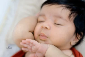 A baby sleeping with hands pose on his face.