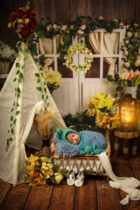 A baby sleeping near by teepee with flowers and a teddy bear.