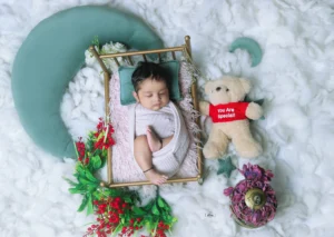 A baby is laying in a crib with a teddy bear and flowers.