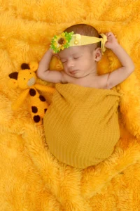 A baby sleeping on a yellow blanket with a giraffe stuffed animal.