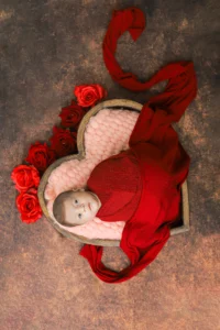 A baby is laying in a heart shaped frame with roses.