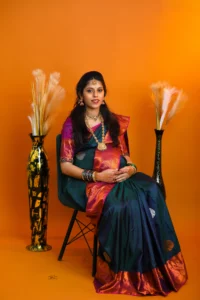 A pregnant woman posing on chair in a sari on an orange background.