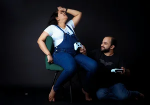 A pregnant woman sitting on a chair and holding a video game controller poses with her husband