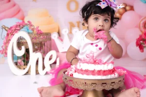 A cute little girl with beautiful eye in pink sitting in front of a cake.