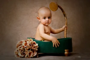 A baby is sitting in a green tub with a wooden stick.