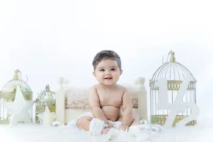 A baby sitting on a white blanket with cute smile